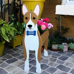 Basenji-shaped dog planter with a blue name tag on a stone patio surrounded by potted plants