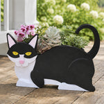 Lying cats planter filled with fresh flowers is placed in the garden
